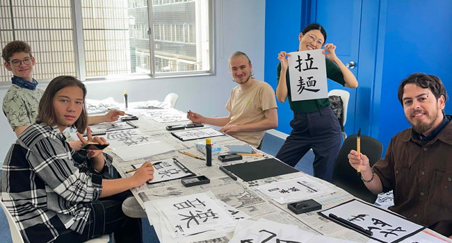 Language study holidays Tokyo Chiyoda with LISA! – Japanese course, writing and cultural learning Adults learning Japanese characters in a class in Tokyo during a LISA! language study holiday practising calligraphy together