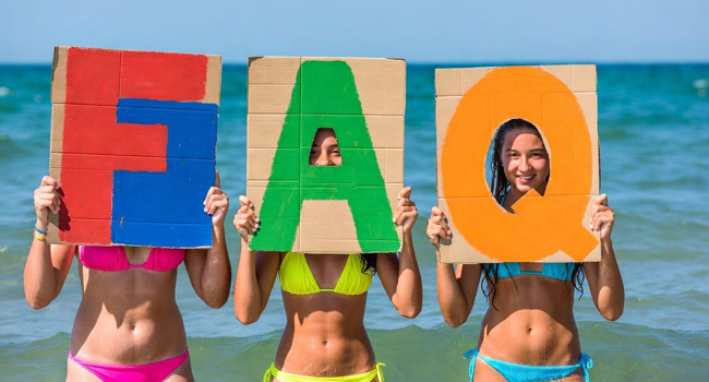 Schoolgirls on the beach in Exmouth holding FAQ letters during a LISA! language study holiday with the sea in the background