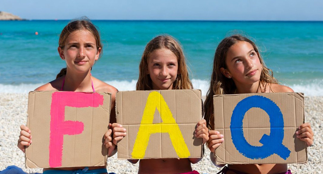 Schoolgirls in Jersey holding FAQ letters on the beach during a LISA! language study holiday with the sea in the background