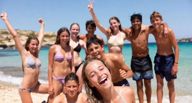 Activity programme during an English language study holiday for students in Malta San Gwann with LISA! Ten teenagers on the beach in Malta San Gwann during the activity programme with raised arms