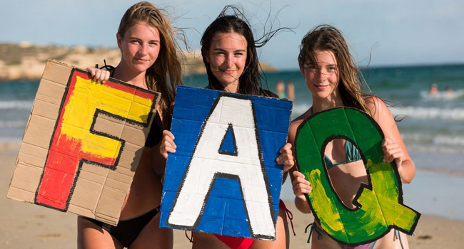 FAQs about student language study holidays in Malta with LISA! – students with letters by the sea Three female students on the beach in Malta holding large FAQ letters during a LISA! language study holiday for students