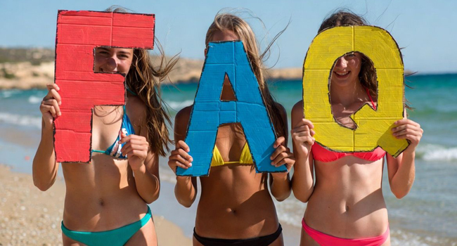 Student language study holiday Malta: FAQs for St Julian’s Three female students on a student language study holiday in Malta at the beach of St Julian’s with large FAQ letters
