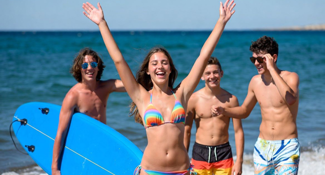 I’m here, Mum: arrived on a language study holiday in Malta with LISA! Girl raises her arms up with three boys and the sea in the background