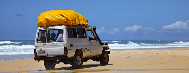Geländewagen fährt entlang des Strandes mit Wellengang im Hintergrund in Australien während einer Sprachreise