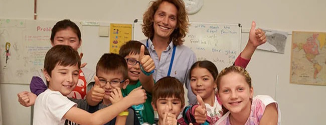 Eine fröhliche Gruppe von Kindern mit ihrem Lehrer im Klassenzimmer bei einer LISA! Sprachreise für Familien